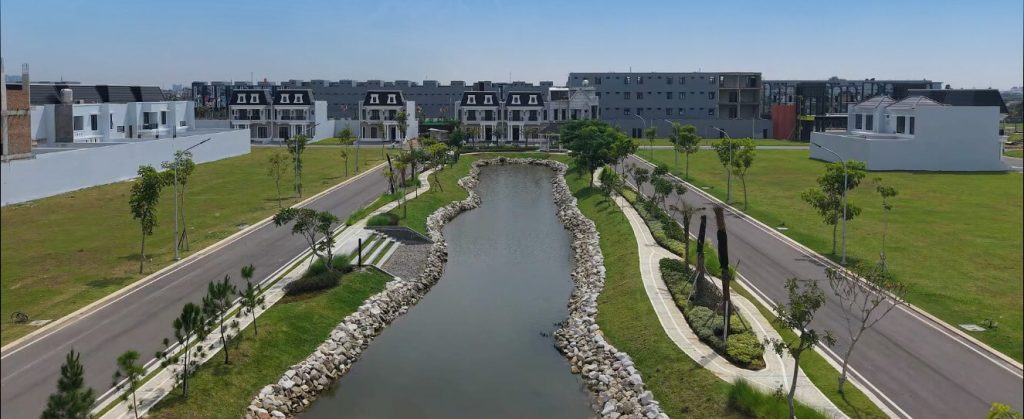 Aerial view of a modern residential community with a central winding water canal, stone borders, and tree-lined walkways on green lawns.