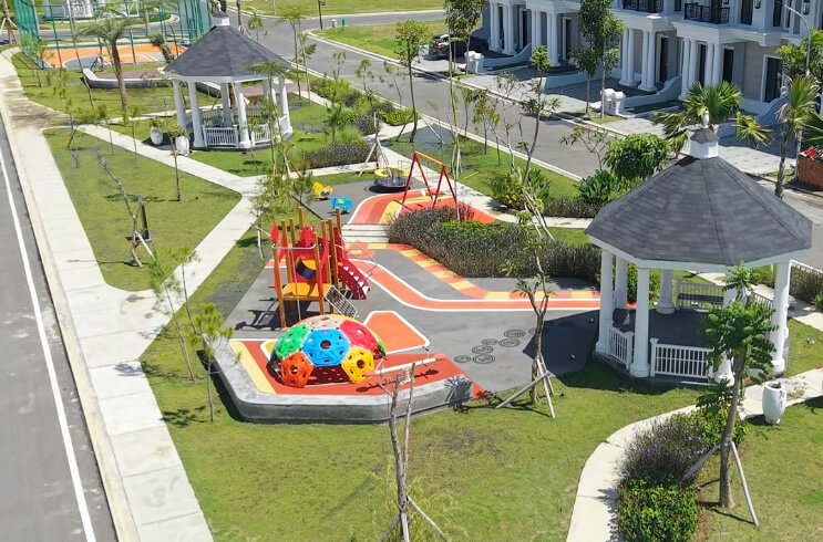 Playground in a residential complex featuring a colorful climbing dome, slide, swings, and two white gazebos with landscaped paths nearby.